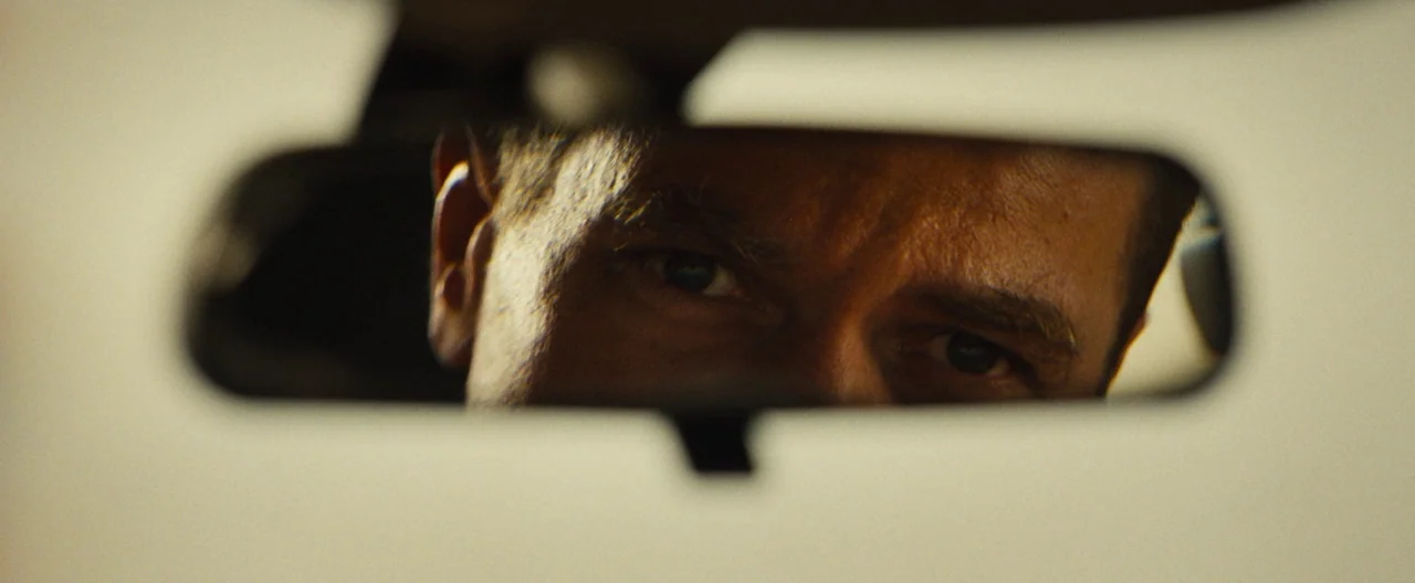 Nocturnal Animals (2016) movie still: closeup — The interior of a vehicle focused on a rearview mirror. A man gazes directly forward from the…