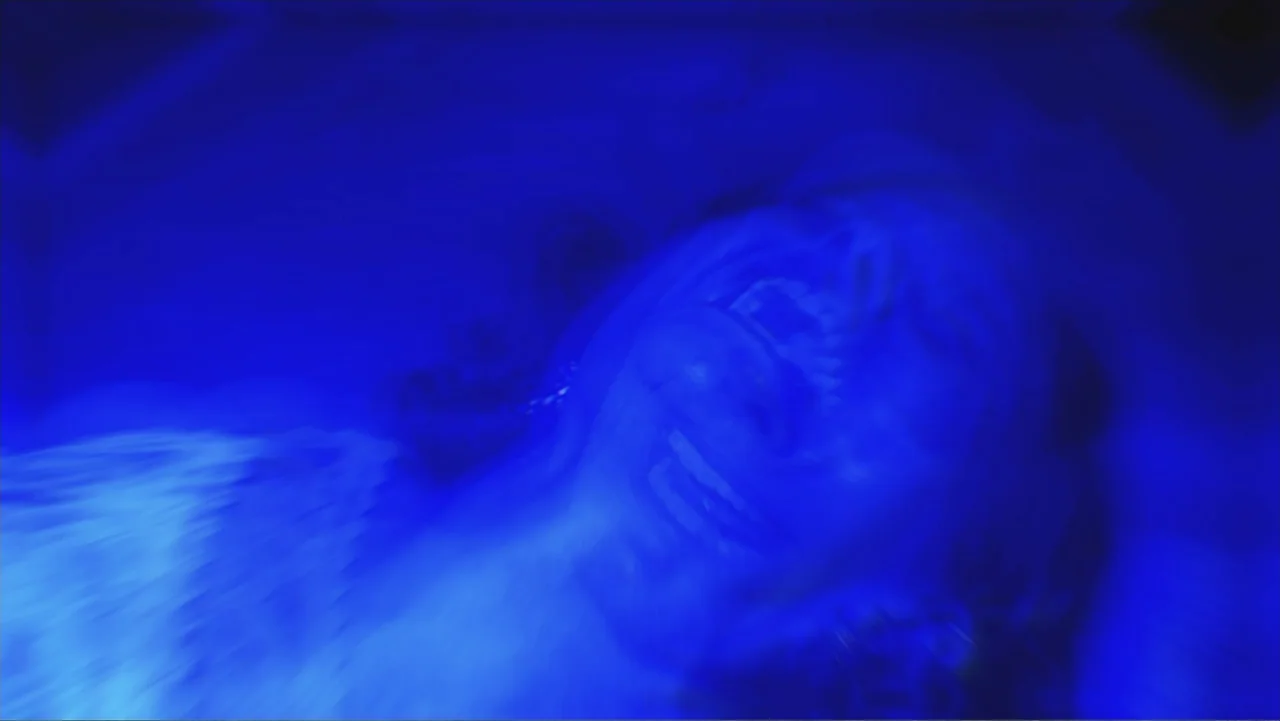 Alien Abduction: Betty and Barney Hill (2022) movie still: closeup — An interior space is enveloped in a monochromatic blue light wash. A woman lies…