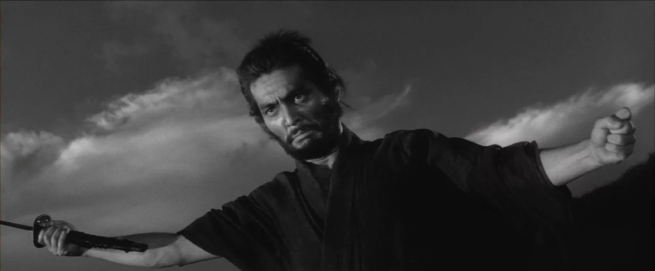 Harakiri (1962) movie still: medium — An outdoor field is visible against a cloudy sky backdrop. A man in a dark kimono holds a sword with his right…