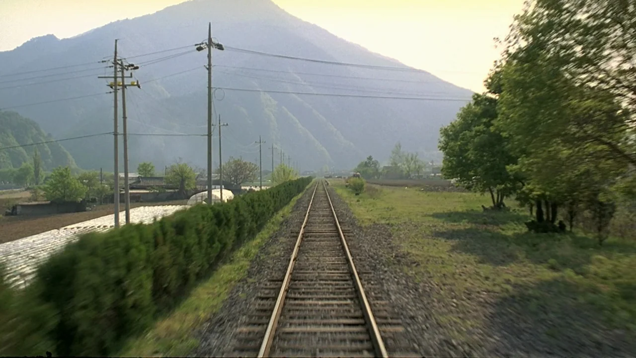 Peppermint Candy (1999) movie still: establishing — Straight train tracks stretch through a rural valley bordered by trees and hills. Power lines…