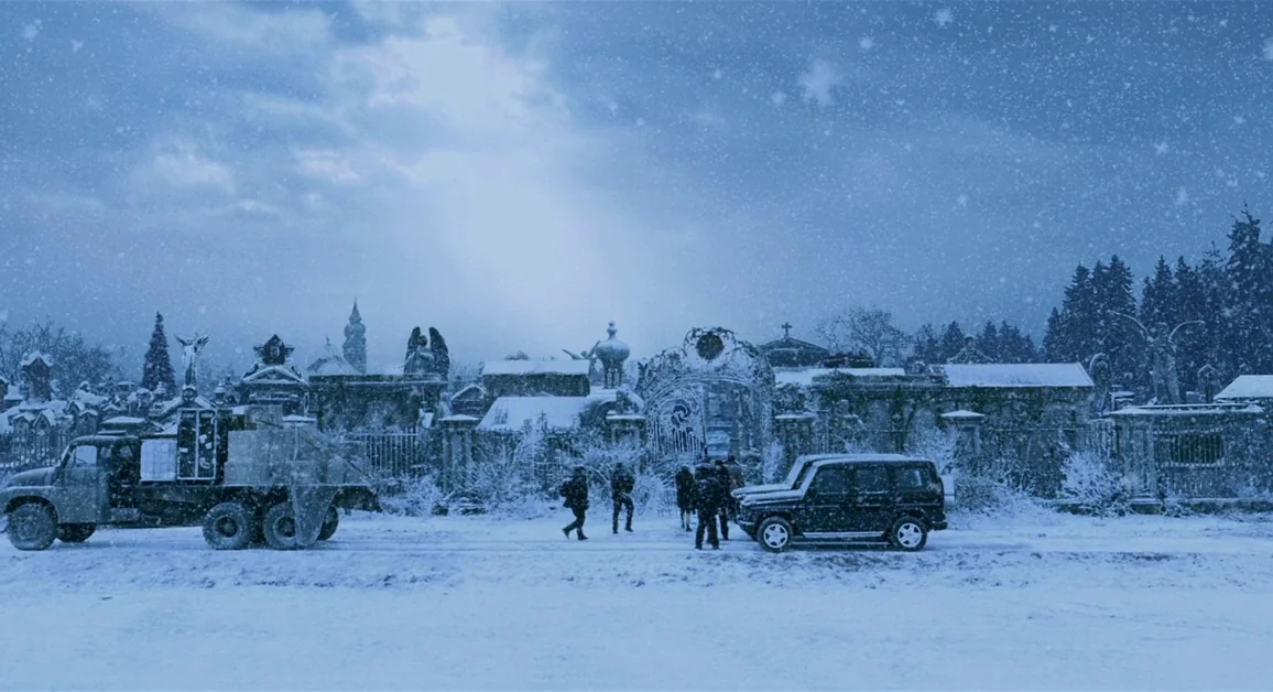 Hellboy (2004) movie still: wide — An ornate gated cemetery is covered in a thick blanket of winter snow. Several figures walk on the snowy ground…