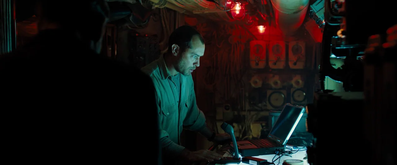 Black Sea (2014) movie still: medium — A cramped and cluttered compartment contains old communication equipment and pipes along the ceiling. A man…