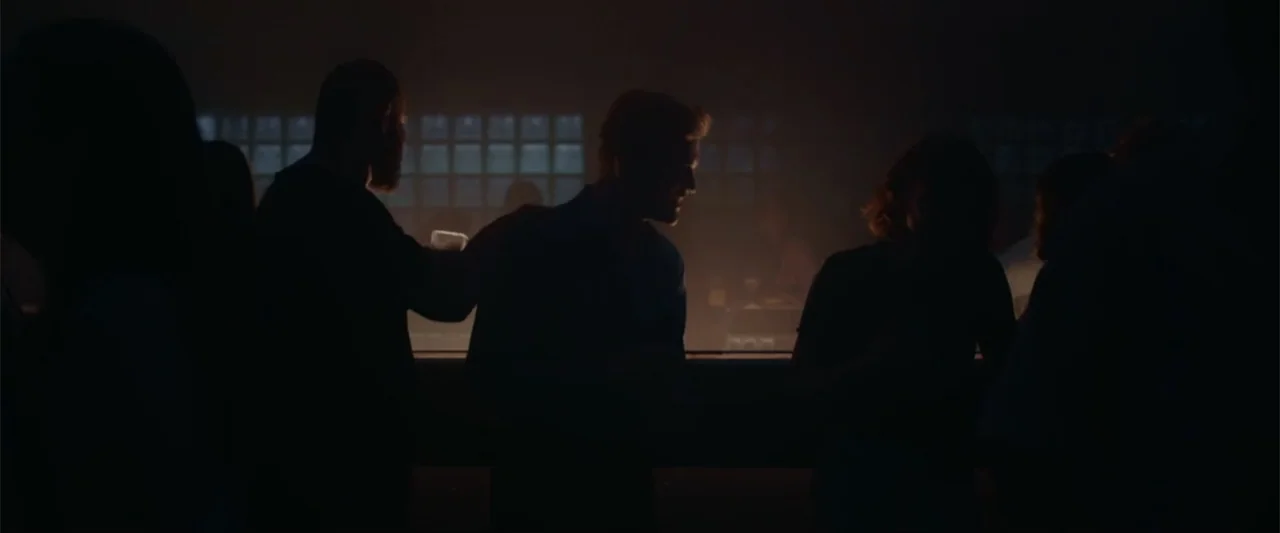 Peacock (2010) movie still: medium — A dimly lit bar with patrons standing along a dark wooden service counter. The subjects are positioned in…