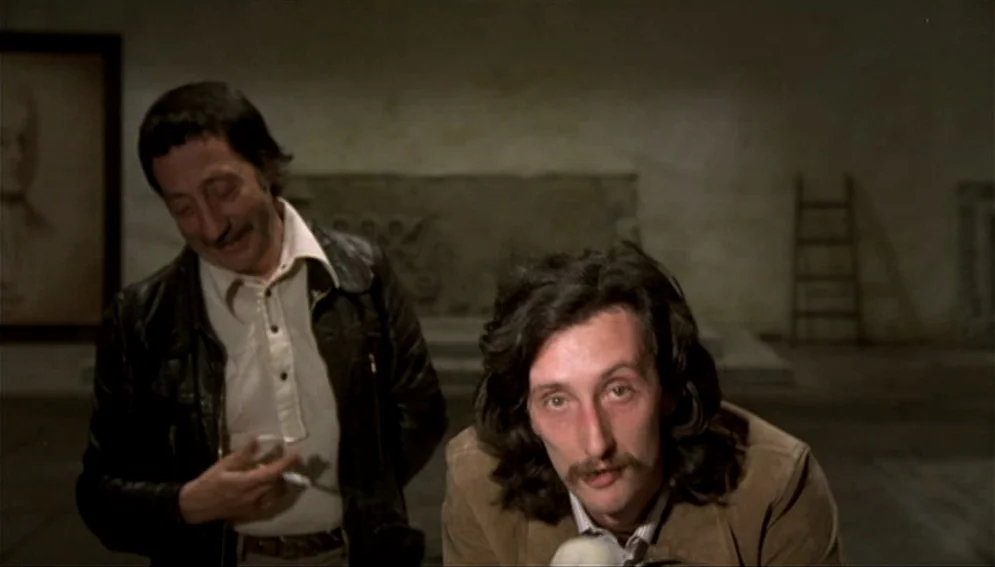 Orchestra Rehearsal (1978) movie still: medium — A stone-walled interior with a wooden ladder propped against a wall. Two men in casual 1970s attire…