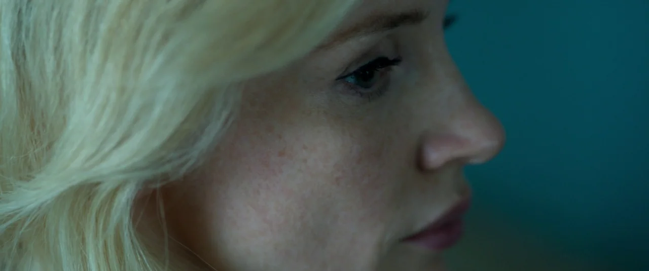 Mother’s Instinct (2024) movie still: closeup — A close-up of a blonde woman's face shown in side profile against a dark background. She looks…