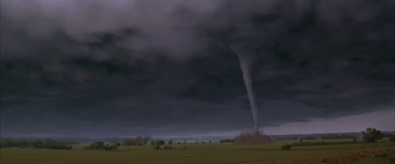 Twister (1996) movie still: establishing — A dark tornado funnel descends from a thick blanket of storm clouds. The funnel touches down in a wide…