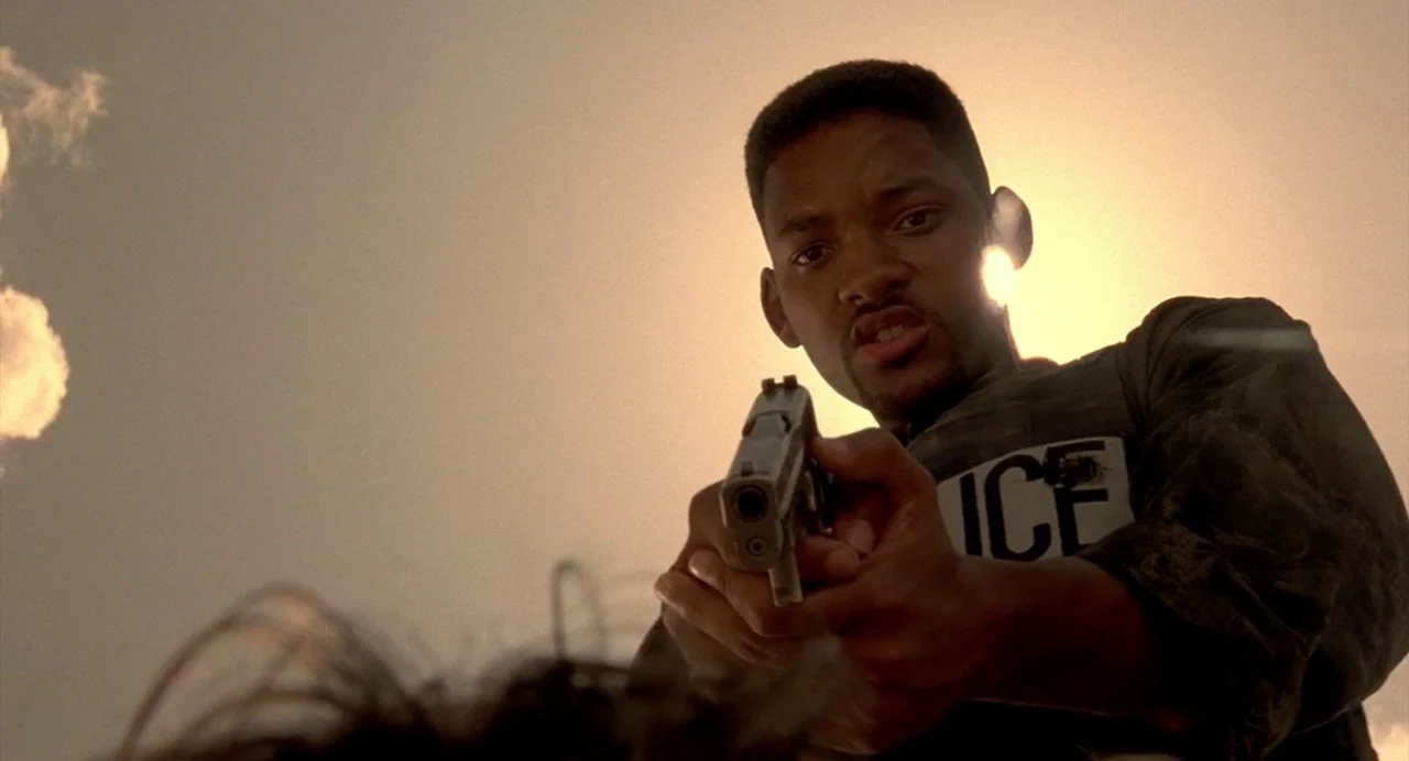 Bad Boys (1995) movie still: medium — A figure stands against a bright, hazy sky during a daytime exterior scene. The man aims a handgun directly…