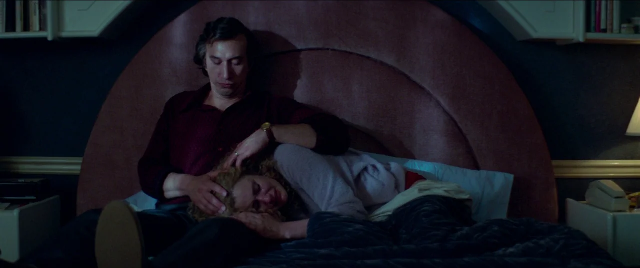 White Noise (2022) movie still: medium — A dimly lit bedroom features a large circular headboard behind a neatly made bed. A man in a dark shirt…