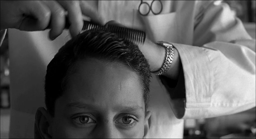 The Man Who Wasn’t There (2001) movie still: closeup — A close-up shot of a young boy receiving a haircut in a professional environment. The…