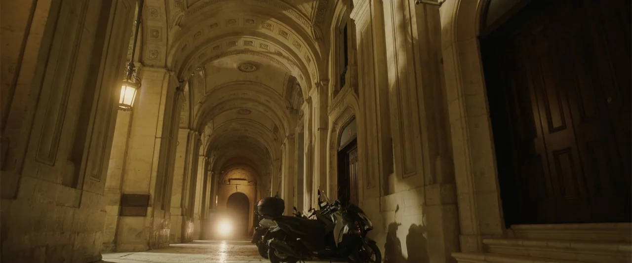Hounds of War (2024) movie still: establishing — An arched stone colonnade features vaulted ceilings and classical architectural carvings. Two…