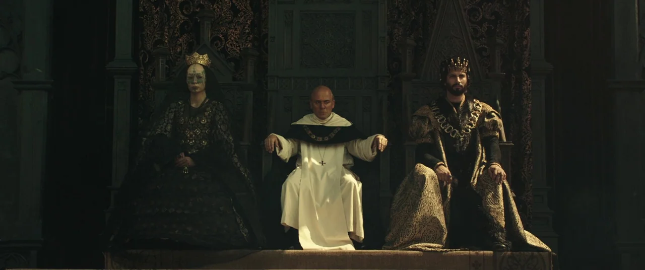 Assassin’s Creed (2016) movie still: wide — A dark, ornate hall features three elaborate chairs placed on a raised dais. A queen, a monk, and a king…
