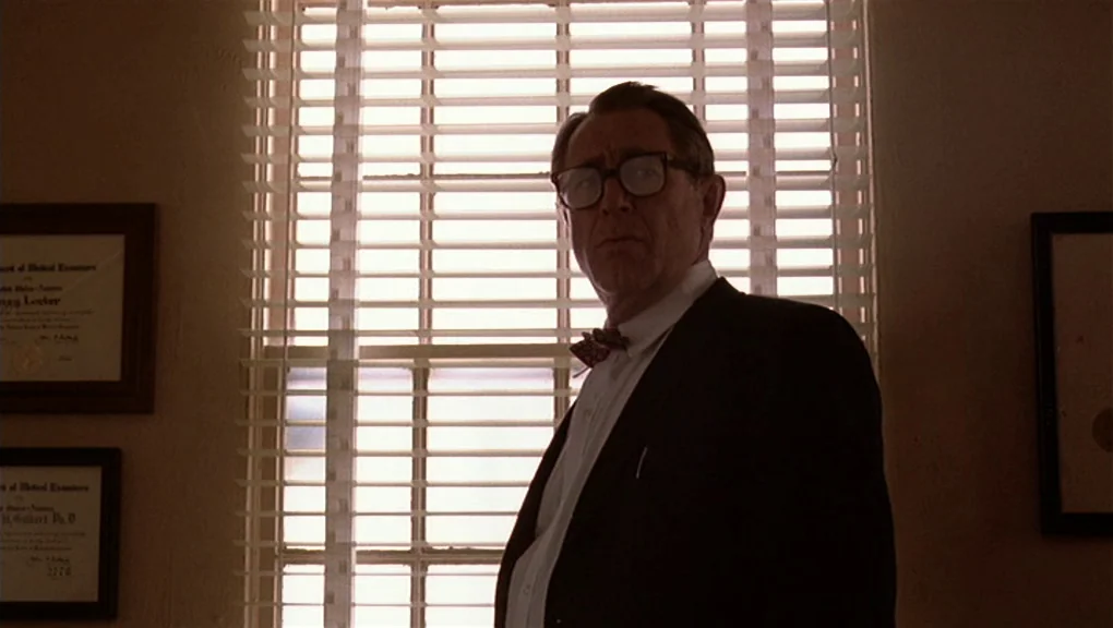 Bird (1988) movie still: medium — An office interior features framed documents on walls flanking a large window with blinds. An older man in a suit…