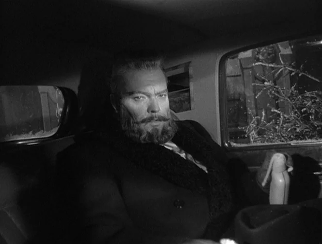 Mr. Arkadin (1955) movie still: medium — A man sits in the dark interior of a car at night. He is facing the camera directly while positioned inside…