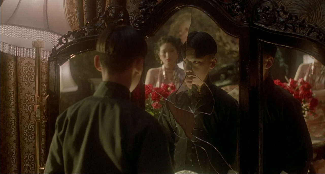 Shanghai Triad (1995) movie still: medium — An opulent room with ornate furniture contains a large vanity featuring a cracked mirror. A young man…