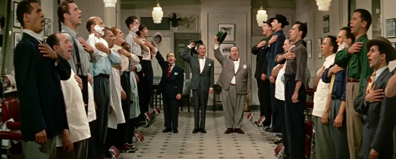 Guys and Dolls (1955) movie still: wide — A spacious barbershop features tiled floors, rows of red chairs, and framed pictures. Many men in suits…