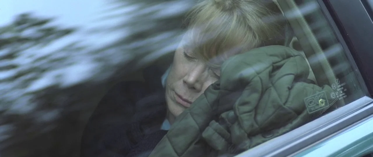 In the Bedroom (2001) movie still: closeup — The interior of a moving vehicle shows an elderly woman leaning against the window. She sleeps with her…