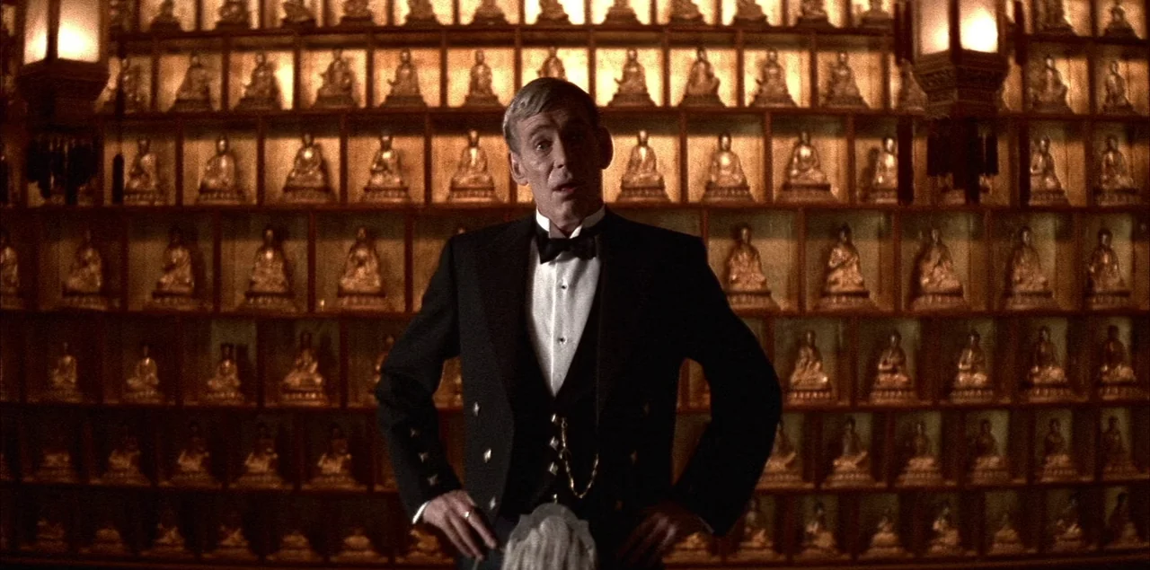 The Last Emperor (1987) movie still: medium — A wall is lined with hundreds of small golden statues in individual wooden cubicles. A man wearing a…