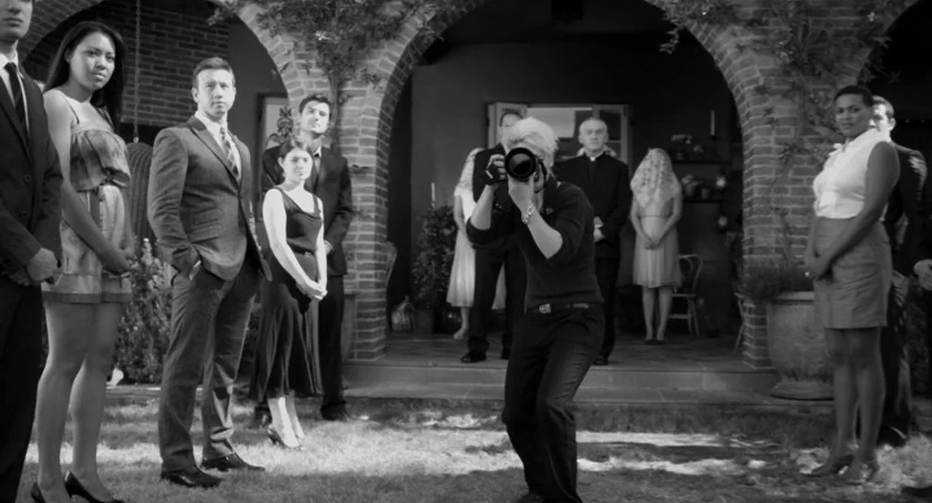 Much Ado About Nothing (2012) movie still: fullbody — A stone courtyard with brick arches features a group of people standing in line. A…