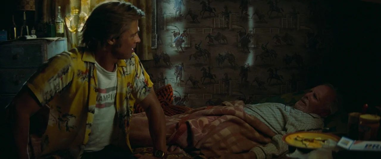 Once Upon a Time… In Hollywood (2019) movie still: medium — A dark bedroom features wallpaper with a cowboy pattern and a bed covered by a blanket.…
