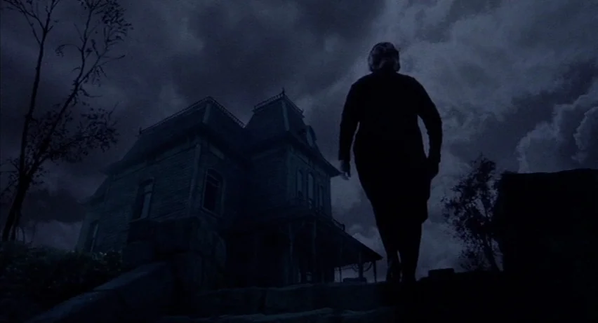 Psycho 2 (1983) movie still: wide — A dark house with Victorian architecture looms under a heavy, clouded night sky. A woman walks up the stone…