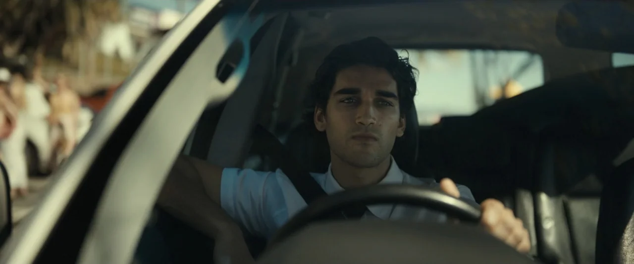 Dangerous Animals (2025) movie still: medium — A man drives a car during the day with blurred exterior surroundings visible. The man focuses forward…