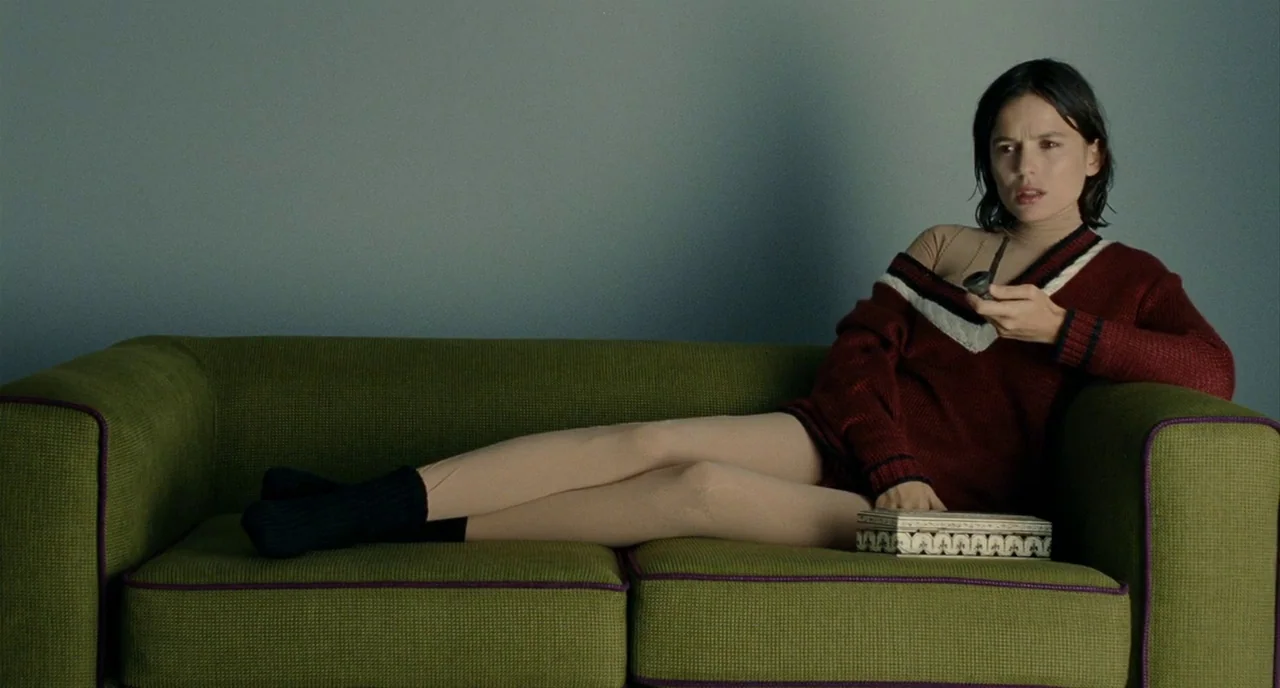 The Skin I Live In (2011) movie still: medium — A woman reclines on a lime green sofa against a solid grey wall. She is positioned horizontally in…