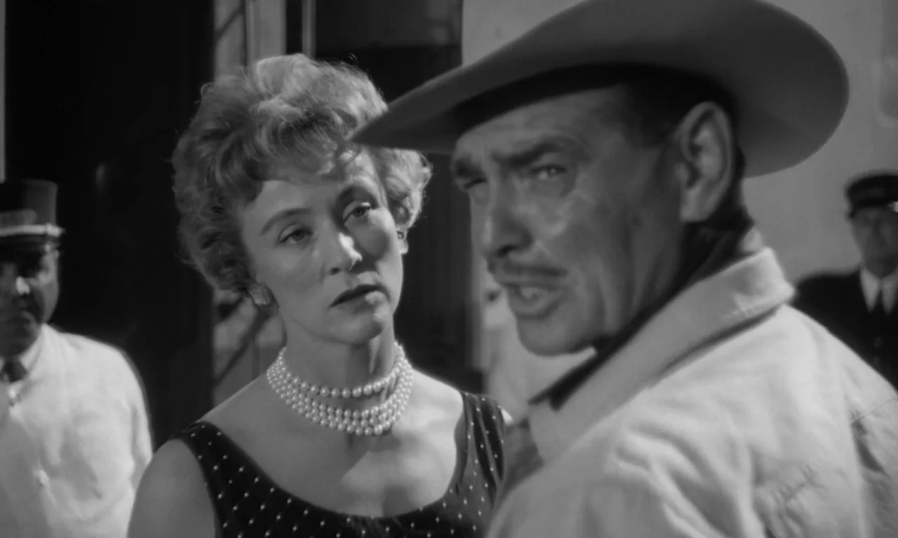 The Misfits (1961) movie still: medium — A public transportation platform features two individuals in the foreground and conductors behind them. A…