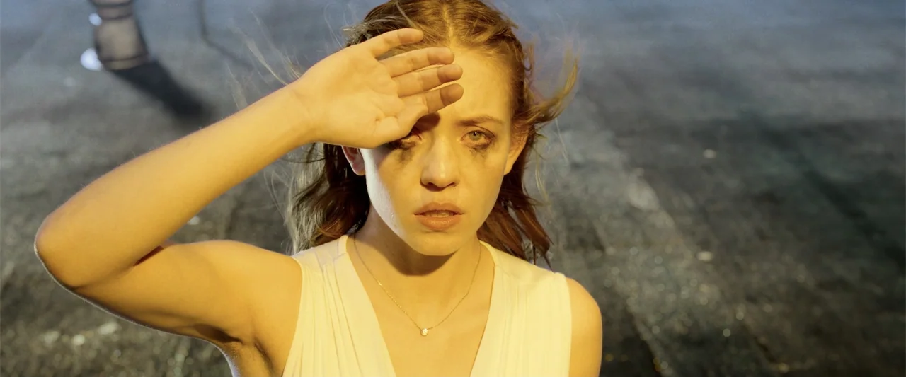 Nocturne (2020) movie still: closeup — An asphalt surface at night serves as the backdrop for a close-up encounter. A young woman with smeared…