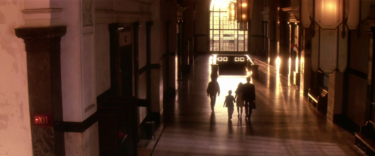 JFK (1991) movie still: wide — A grand terminal lobby features high ceilings and a wall of large windows. Four individuals walk away from the viewer…