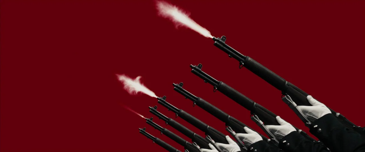The Spirit (2008) movie still: medium — A row of rifles is pointed upward against a flat, solid dark red background. Each rifle barrel emits a plume…
