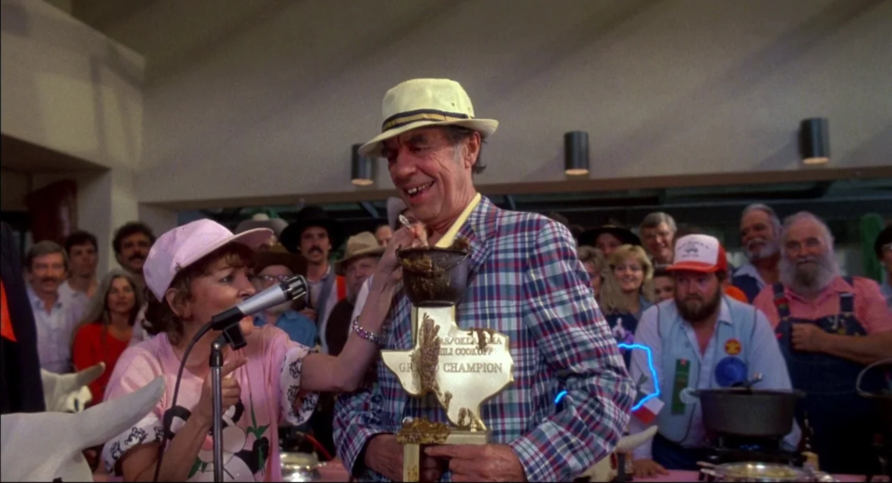 The Texas Chainsaw Massacre 2 (1986) movie still: medium — An indoor community gathering features a crowd of people watching an award ceremony. A…