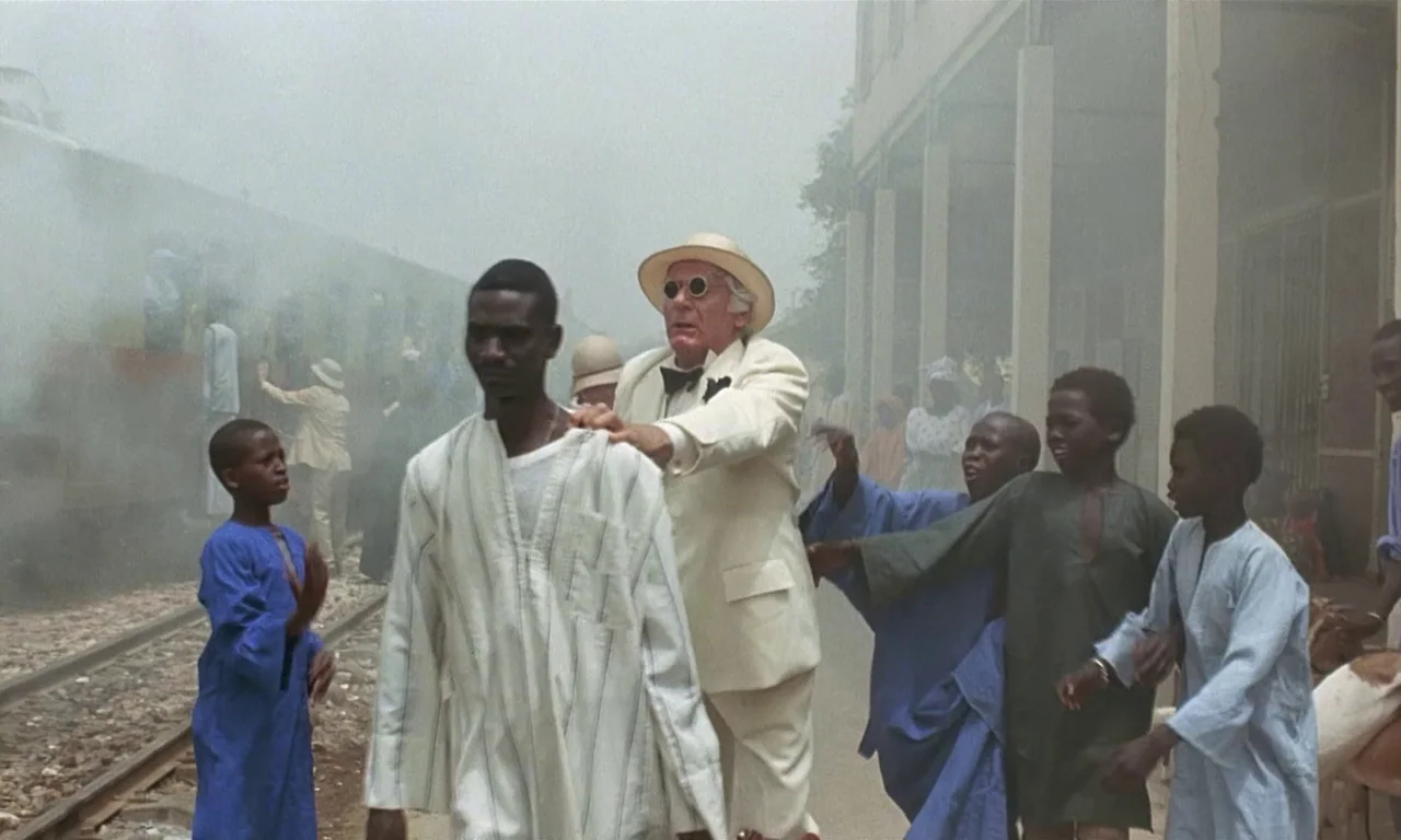 Coup De Torchon (1981) movie still: fullbody — A dusty railway platform with a train arriving in thick haze and concrete architecture. A white man…
