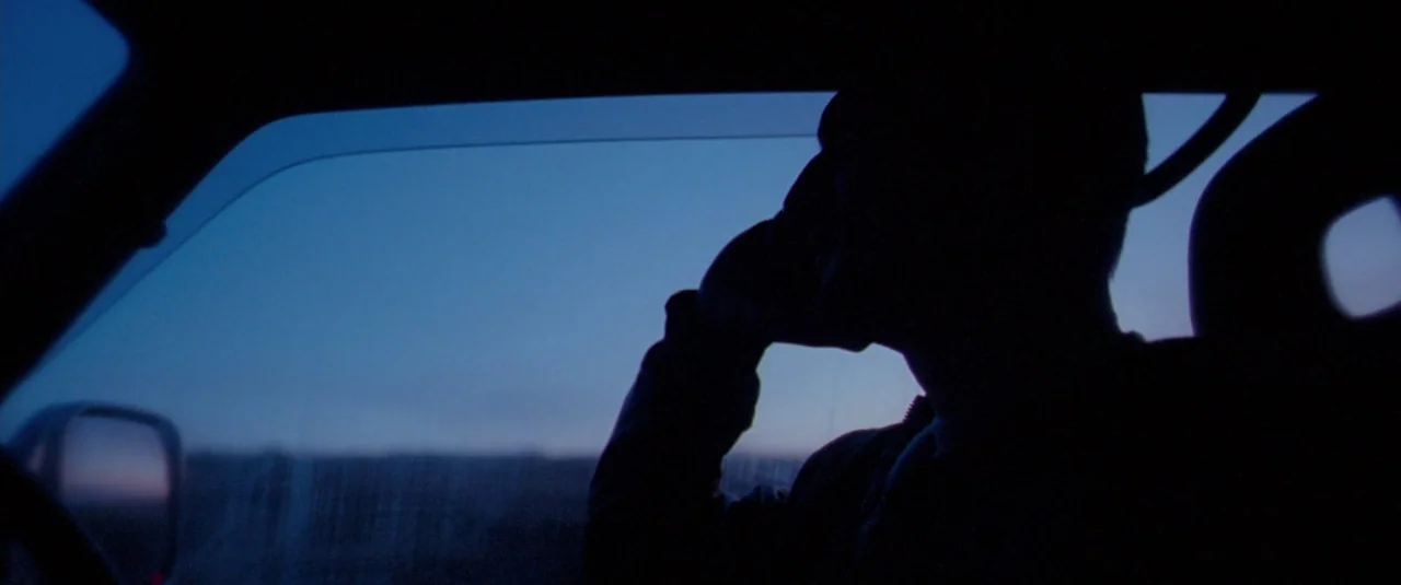 Catch Me Daddy (2014) movie still: medium — The interior of a car at dusk with an unlit cabin. A man in silhouette holds a phone to his ear while…