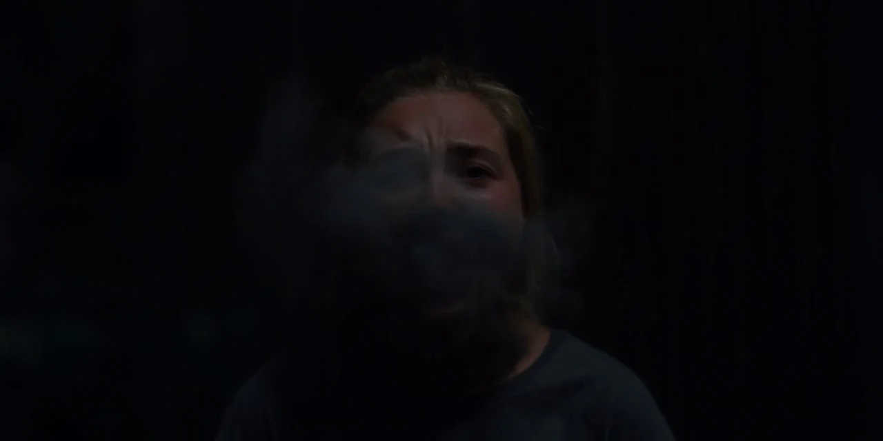 Midsommar (2019) movie still: closeup — A dark, underexposed space lacks architectural detail or defining background elements. A young woman exhales…