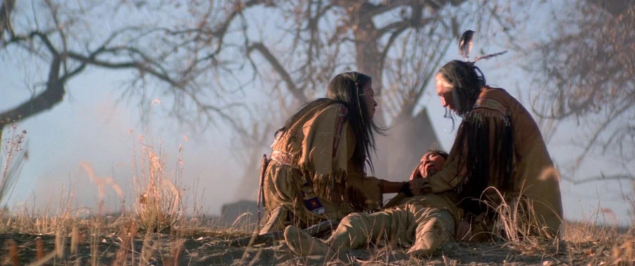 Dances With Wolves (1990) movie still: medium — A dry, grassy prairie field features large bare trees in the soft daylight. Two figures in buckskin…