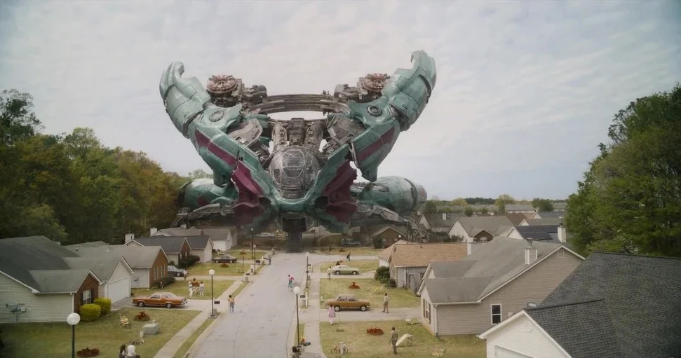 Guardians of the Galaxy Vol. 3 (2023) movie still: establishing — A suburban residential street is lined with single-story homes and parked vintage…