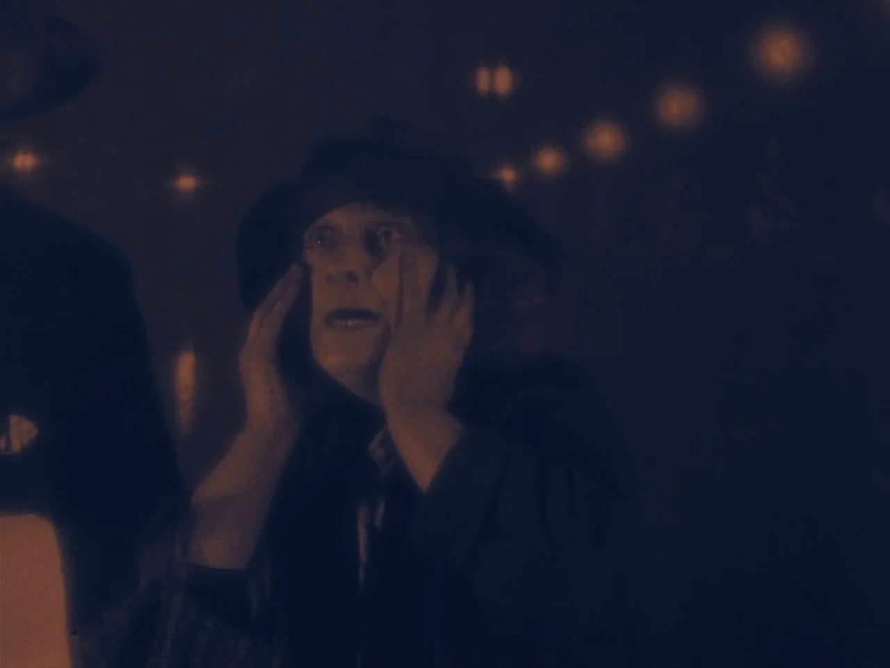 The Lodger (1927) movie still: closeup — A dimly lit interior space with bokeh lights in the background. A woman presses both hands against her face…
