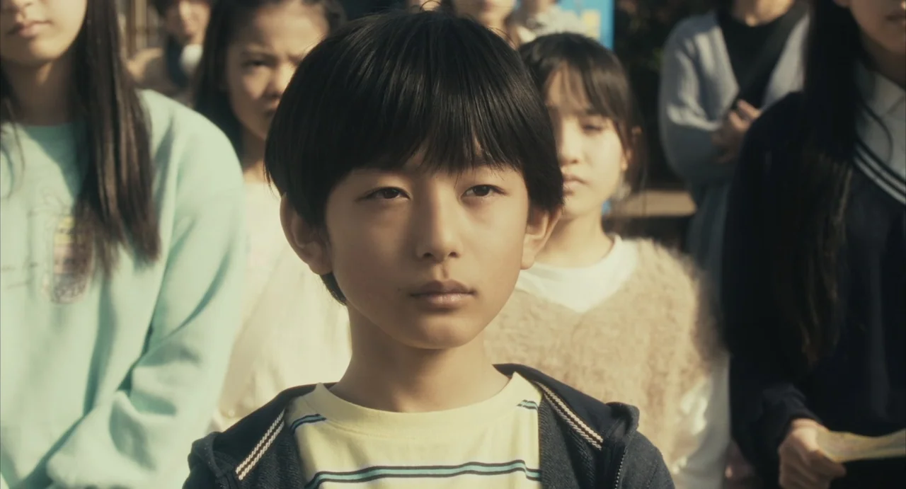 Stigmatized Properties: Possession (2025) movie still: medium — An outdoor schoolyard setting with a group of children standing together during the…