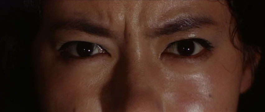 Gate of Flesh (1964) movie still: closeup — A dark, nondescript interior space frames a human face. A woman stares forward with intense, unblinking…