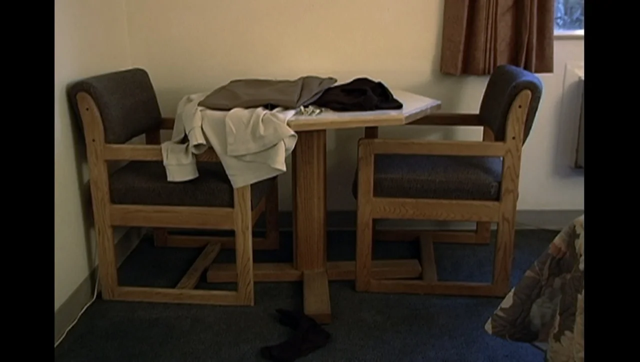 The Trials of Ted Haggard (2009) movie still: medium — A dated hotel corner with two wooden chairs tucked under a small square table. A white…