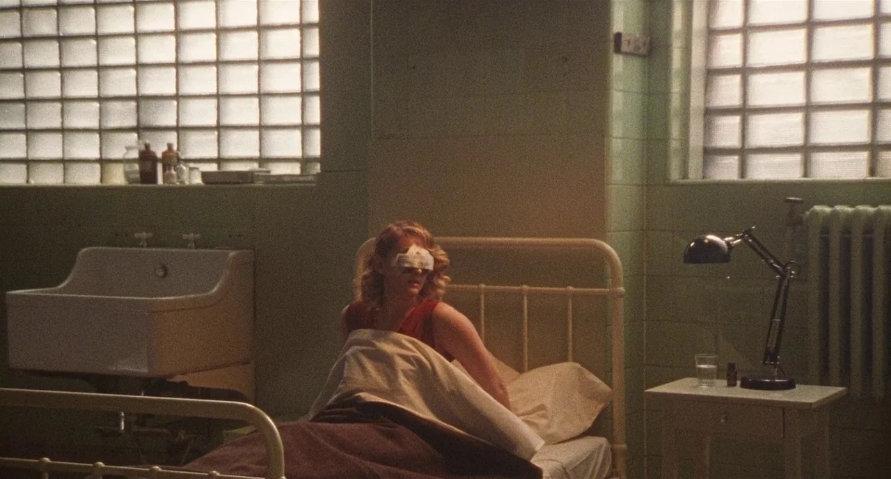 Chained For Life (2018) movie still: medium — A vintage-style room features light green tiled walls and glass block windows. A woman with bandaged…