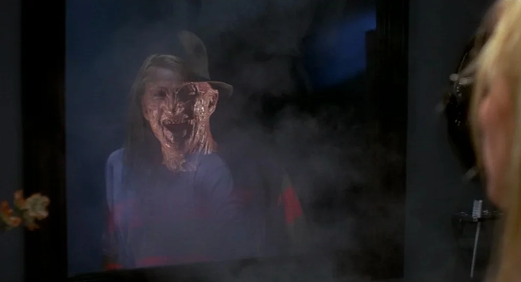 A Nightmare On Elm Street 3: Dream Warriors (1987) movie still: medium — A dimly lit space features a large mirror framed against a dark wall. A…