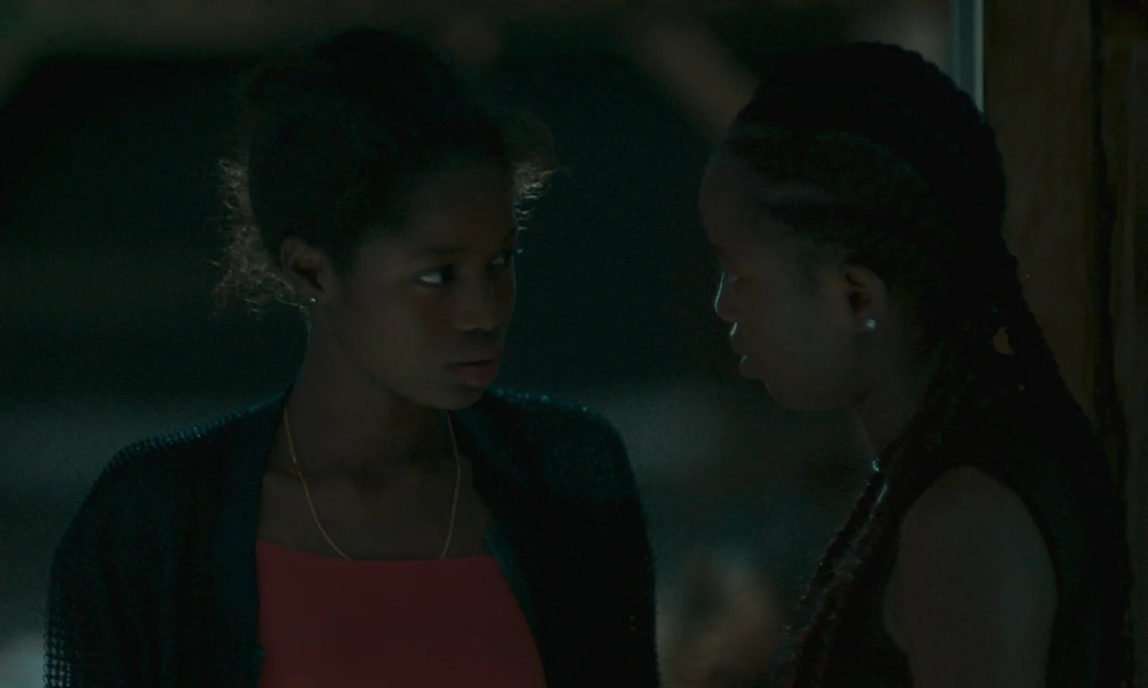 Atlantics (2019) movie still: medium — A dimly lit room with dark surroundings and minimal environmental detail. Two young women stand close…