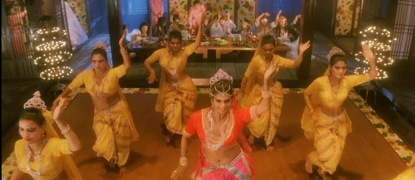 Green Snake (1993) movie still: wide — A group of women in traditional Indian dance attire perform on a wooden floor. The background shows a banquet…