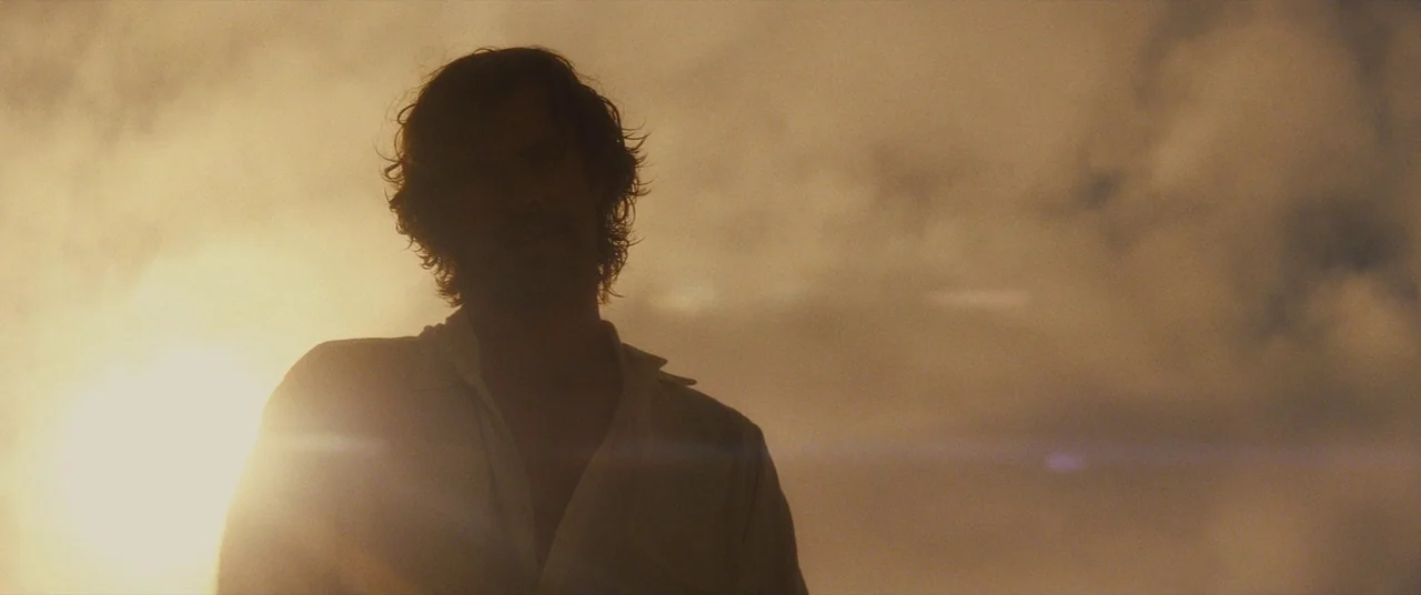 Bad Times at the El Royale (2018) movie still: medium — A man stands outdoors under a bright, hazy sky during the golden hour. The sunlight is…