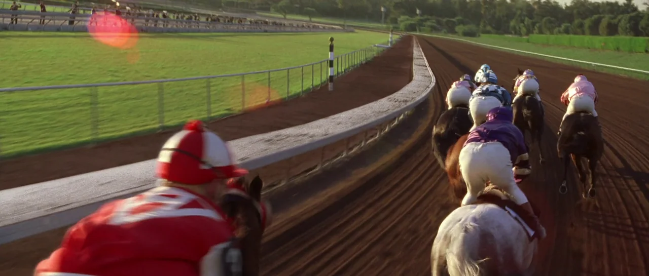 Seabiscuit (2003) movie still: wide — A group of jockeys on horses race along the curve of a dirt track. The track is bordered by a metal railing…