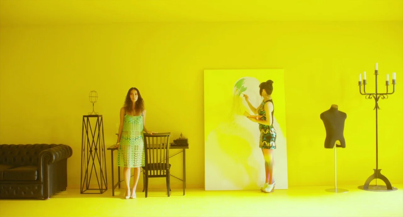 Making of: Antiporno (2016) movie still: wide — A spacious room features walls and floors entirely covered in a bright yellow finish. Two women…