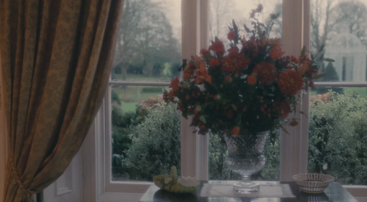 The Deep Blue Sea (2011) movie still: medium — A glass vase with a vibrant orange and red flower arrangement sits on a table. The window frame looks…