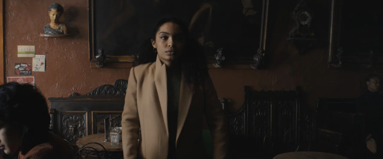 The Sun Is Also a Star (2019) movie still: medium — A dimly lit cafe interior with dark wood paneling and decorative wall portraits. A young woman…