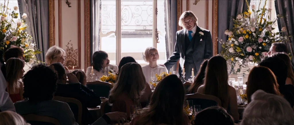 The Look of Love (2013) movie still: medium — An elegant dining room features ornate wall molding and large windows draped in blue. A man in a suit…